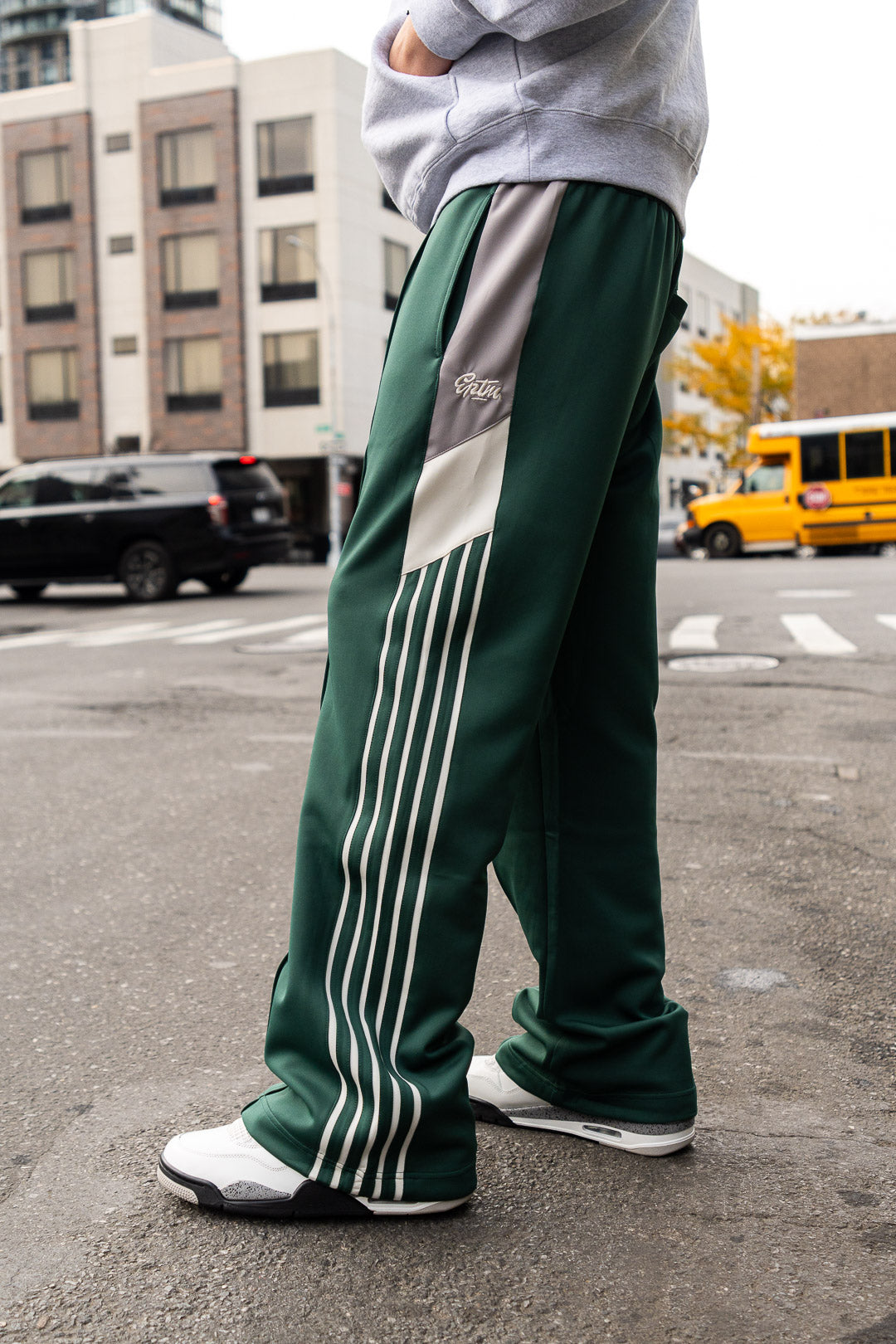 Person wearing green Adidas tracksuit pants on a city street.