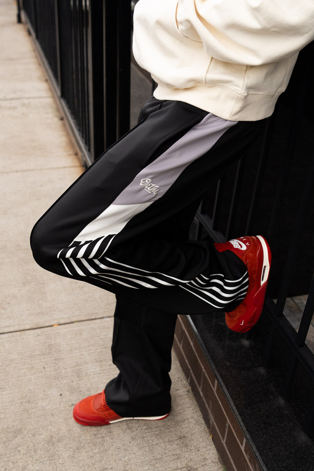 Person wearing black pants with white stripes and red shoes on a sidewalk.